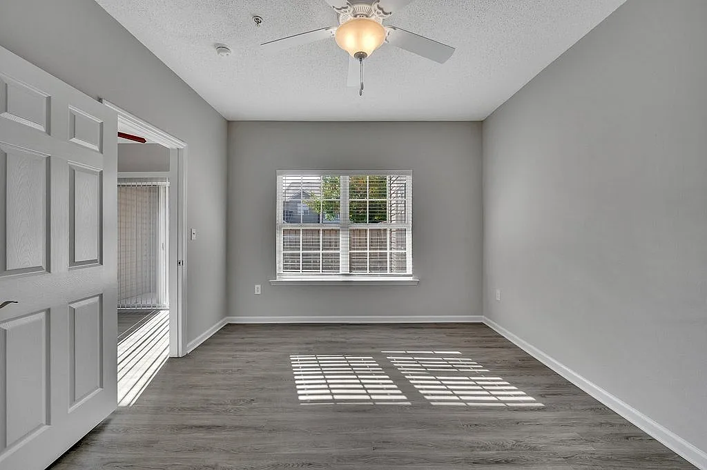 Bright, spacious bedroom with modern ceiling fan, large window, and elegant flooring in a stylish apartment.