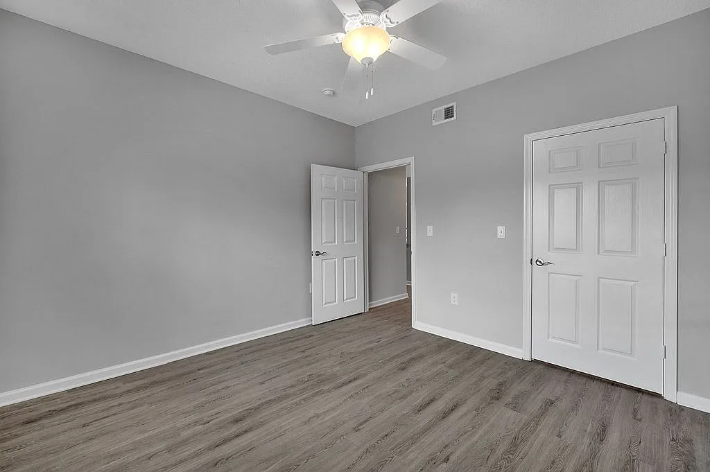 Spacious room with sleek wood flooring and bright, neutral walls, featuring a ceiling fan and double doors, perfect for a serene and versatile living space.