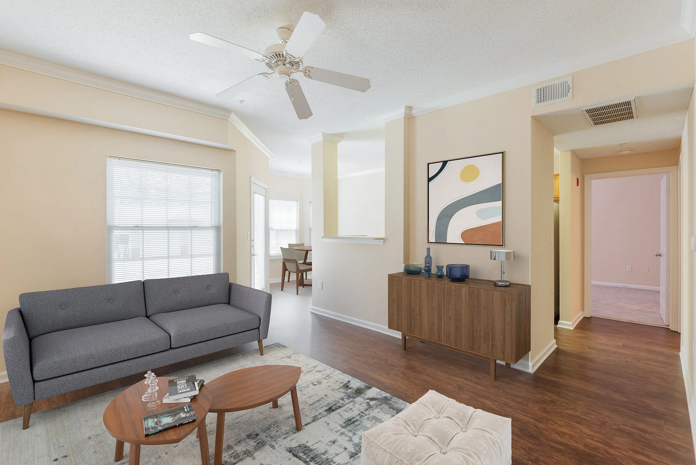 Bright and inviting living area with modern gray sofa, stylish wooden furniture, and abstract wall art, featuring natural light from large windows.