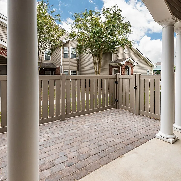 Charming outdoor patio with elegant brick flooring and a privacy fence, surrounded by lush greenery, ideal for relaxation.