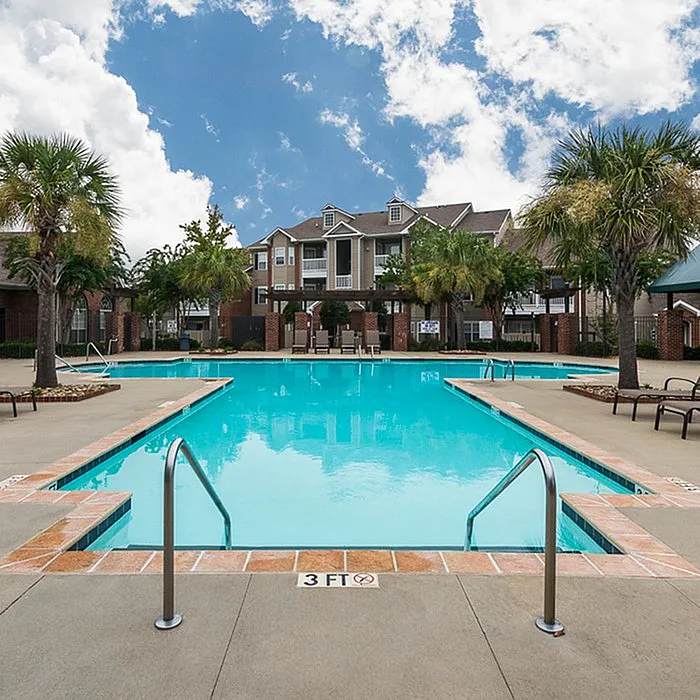 Inviting apartment complex featuring a sparkling swimming pool surrounded by lush palm trees and elegant architecture.