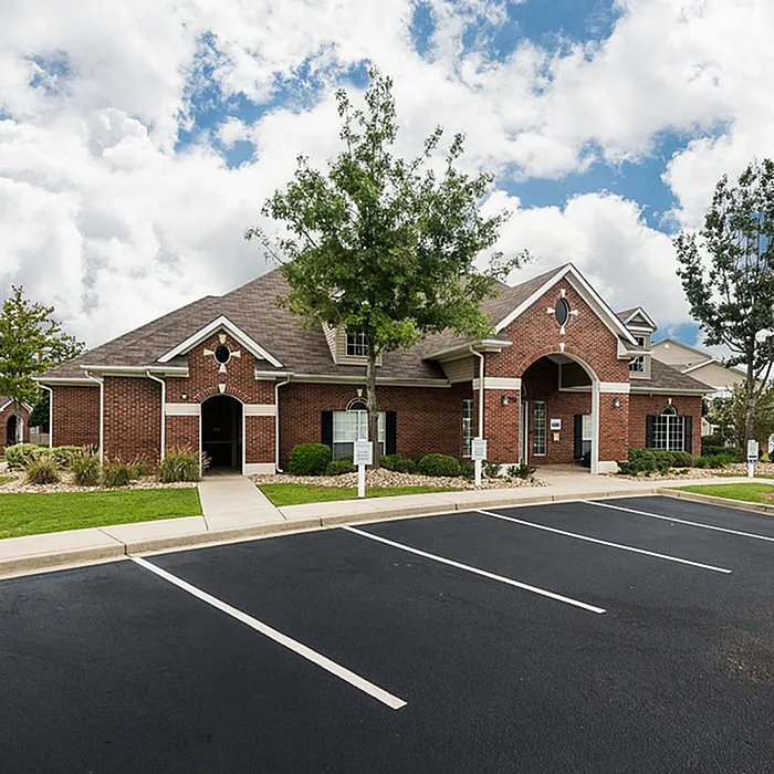 Charming brick apartment complex with lush landscaping and abundant parking, set against a beautiful sky.