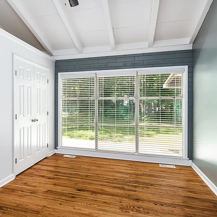 Bright and inviting room with large windows showcasing a lush garden view, complemented by elegant hardwood floors and a vaulted ceiling.