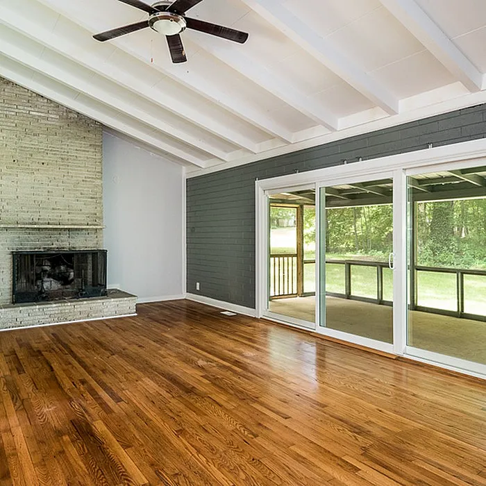 Charming living room with vaulted ceilings, elegant wood flooring, a rustic brick fireplace, and large sliding glass doors opening to a serene outdoor view.
