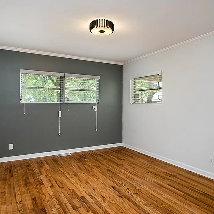 Bright and airy room with elegant hardwood floors, modern light fixture, and large windows offering a view of lush greenery.