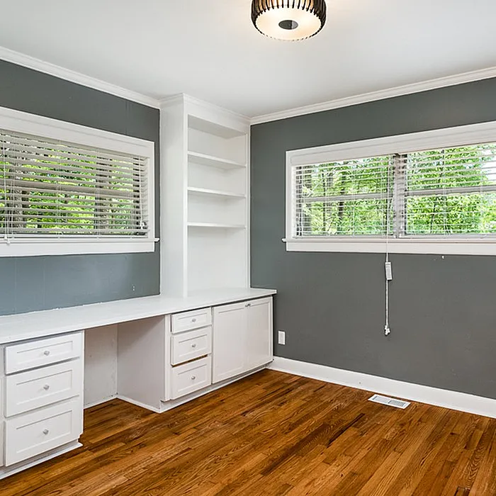 Bright home office with modern built-in desk, ample shelving, and large windows with lush green views.