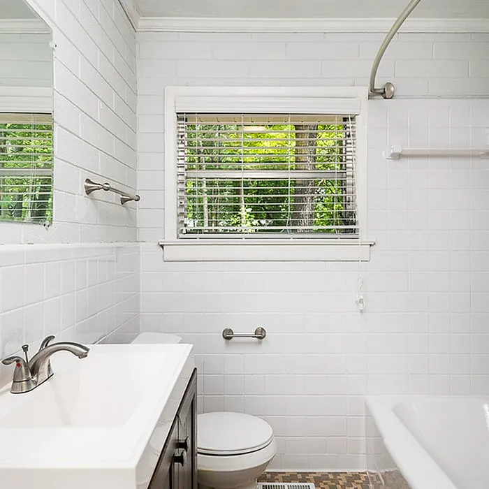 Bright and inviting bathroom with modern fixtures, a large window offering lush greenery views, and elegant white tiles.