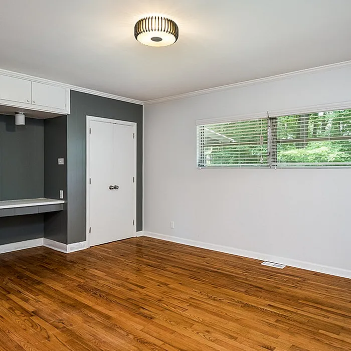 Bright and airy room with polished wooden floors, sleek modern lighting, and large windows offering a serene green view.