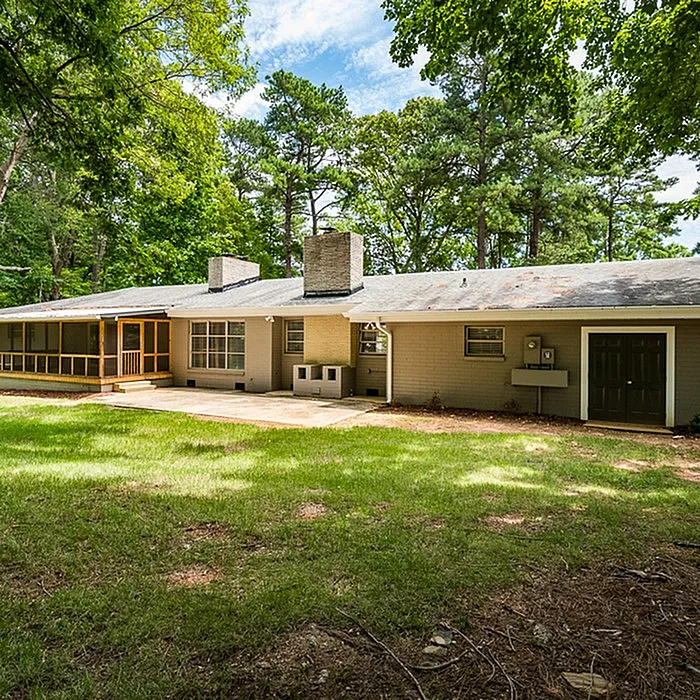 Charming ranch-style home nestled in lush greenery with a spacious front yard and cozy porch, perfect for serene living.