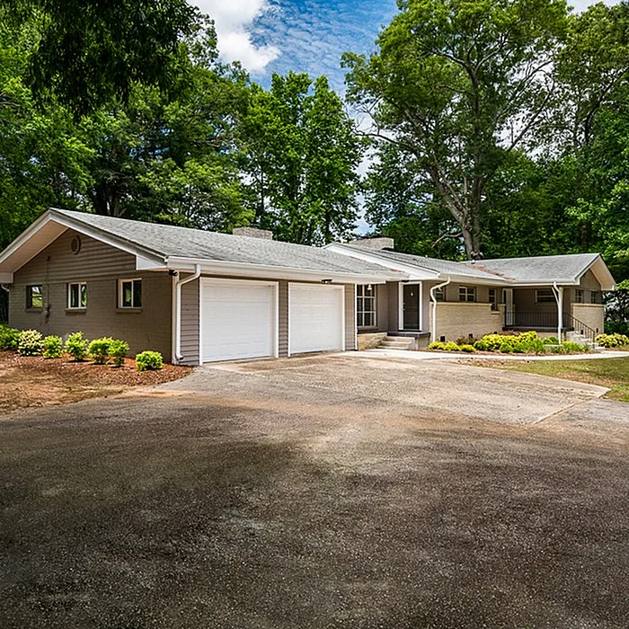Charming ranch-style home with two-car garage, nestled in a lush, green setting with mature trees and beautifully landscaped front yard.
