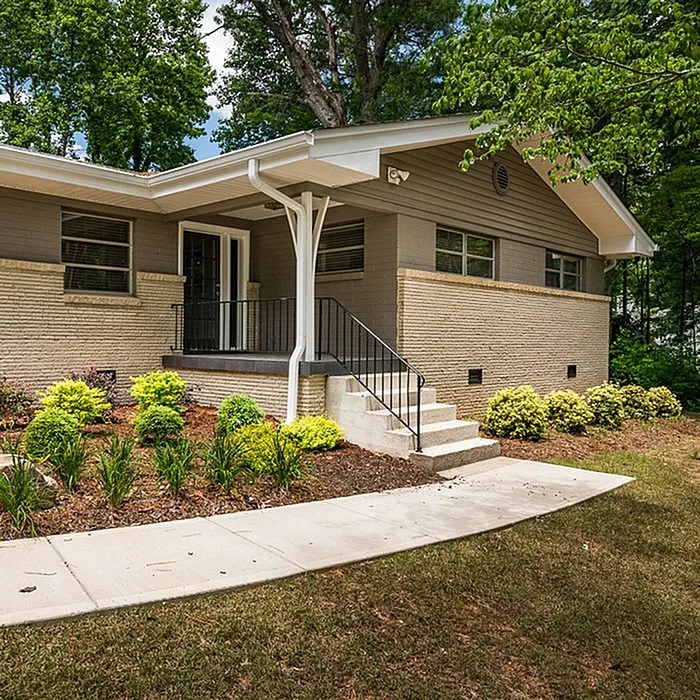 Charming mid-century home with a welcoming entrance, lush landscaping, and modern brick facade, nestled among serene greenery.