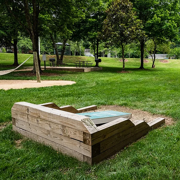 Inviting outdoor space featuring a wooden bench, picnic table, and hammock set amidst lush green lawns and trees, perfect for relaxation and leisure.