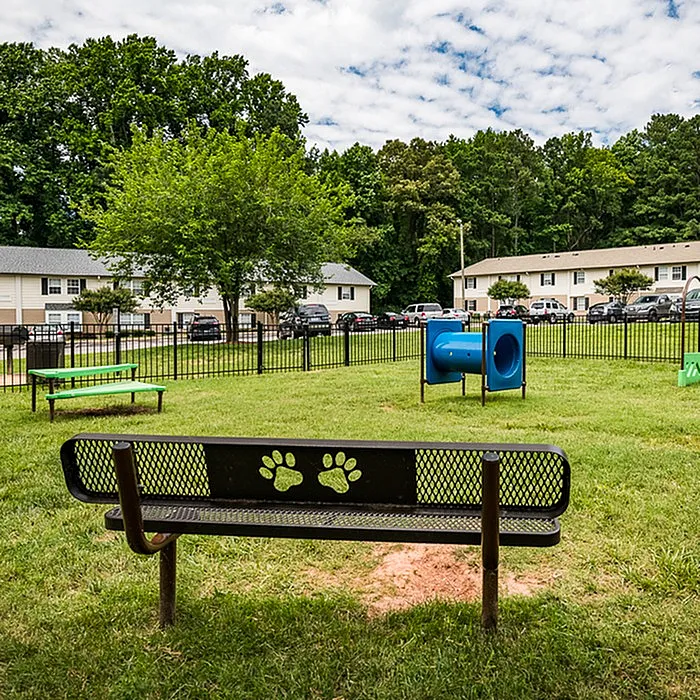 Charming community park with playful paw-print bench, vibrant green spaces, and engaging play equipment, surrounded by cozy residential homes.