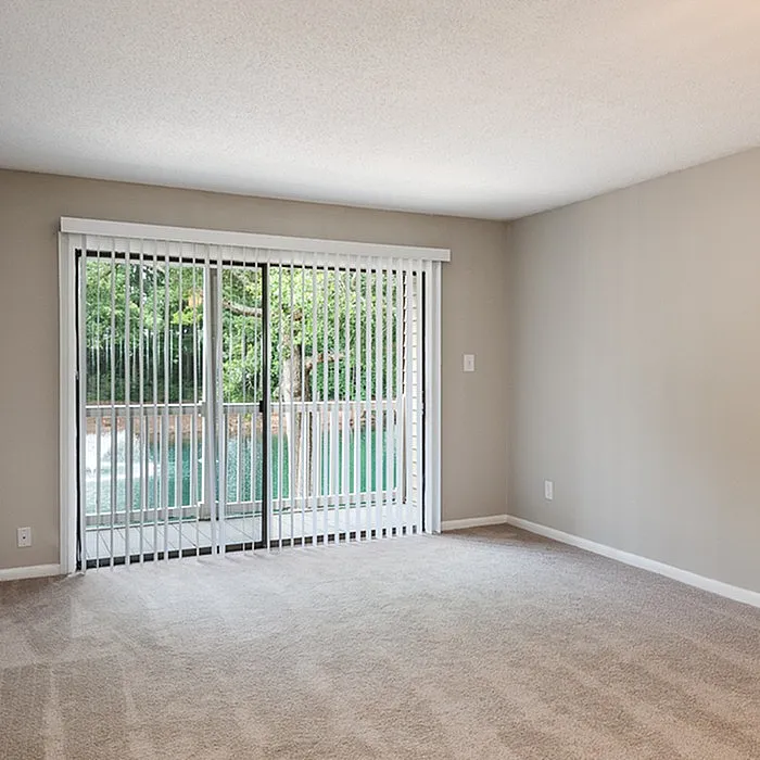 Bright and spacious room with plush carpet and large sliding glass doors offering serene water views.
