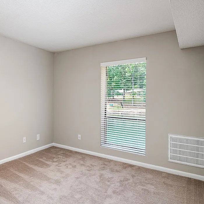 Bright and inviting unfurnished room with a large window, beige walls, and soft carpet flooring, perfect for personalization.