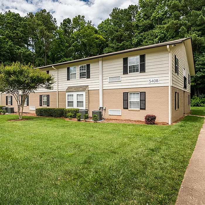 Charming two-story apartment building surrounded by lush greenery, offering a serene and inviting community atmosphere.