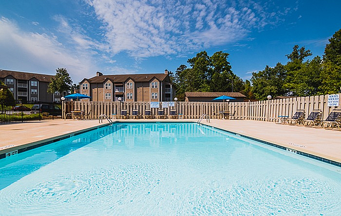 Inviting outdoor pool area with crystal clear water, surrounded by charming apartment buildings and lush greenery under a sunny blue sky.