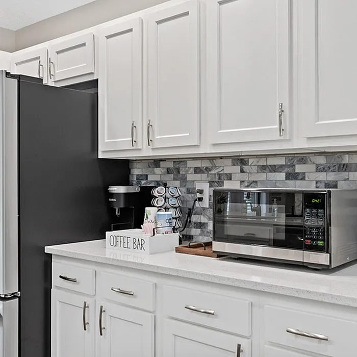 Elegant kitchen with sleek white cabinets, modern appliances, and a stylish coffee bar on a polished countertop.