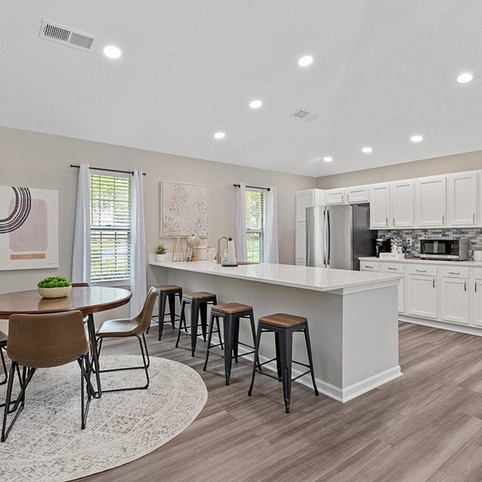 Modern open-concept kitchen and dining area with sleek white cabinets, stainless steel appliances, and elegant wooden flooring.