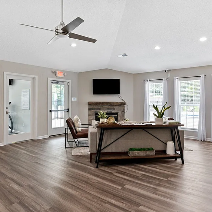 Modern living room with sleek hardwood floors, stylish ceiling fan, and abundant natural light from large windows, featuring a cozy sofa and wall-mounted TV.