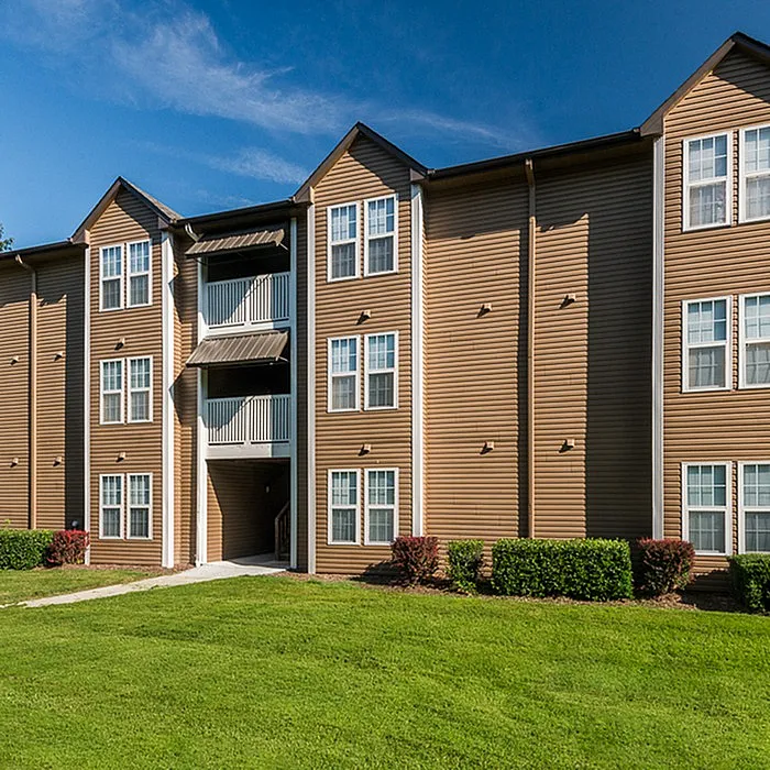 Charming apartment building with modern brown exterior and lush green lawn under a clear blue sky.