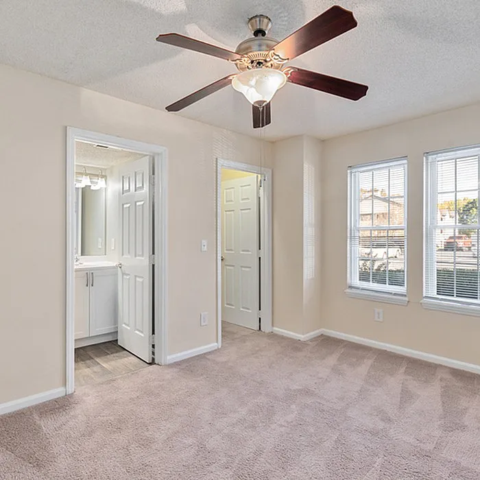 Bright and airy bedroom with plush carpeting, ceiling fan, and large windows; attached modern bathroom for convenience.
