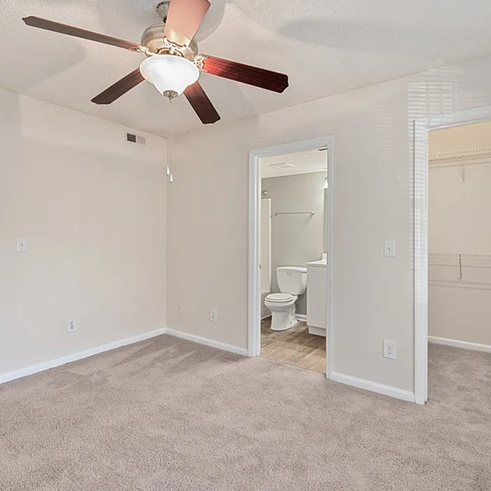 Bright bedroom with plush carpet, ceiling fan, and direct access to a modern en-suite bathroom and spacious closet.