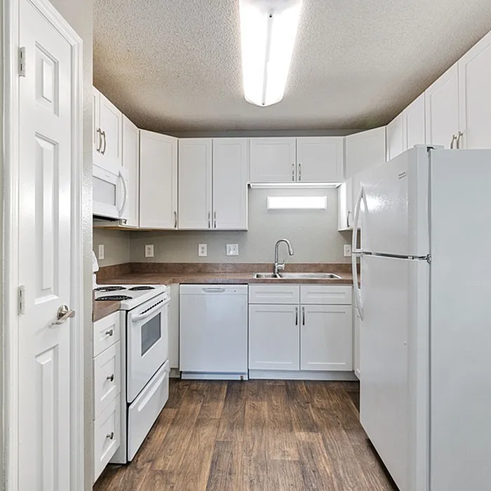 Modern kitchen with sleek white cabinetry, stainless appliances, and rich wood flooring.
