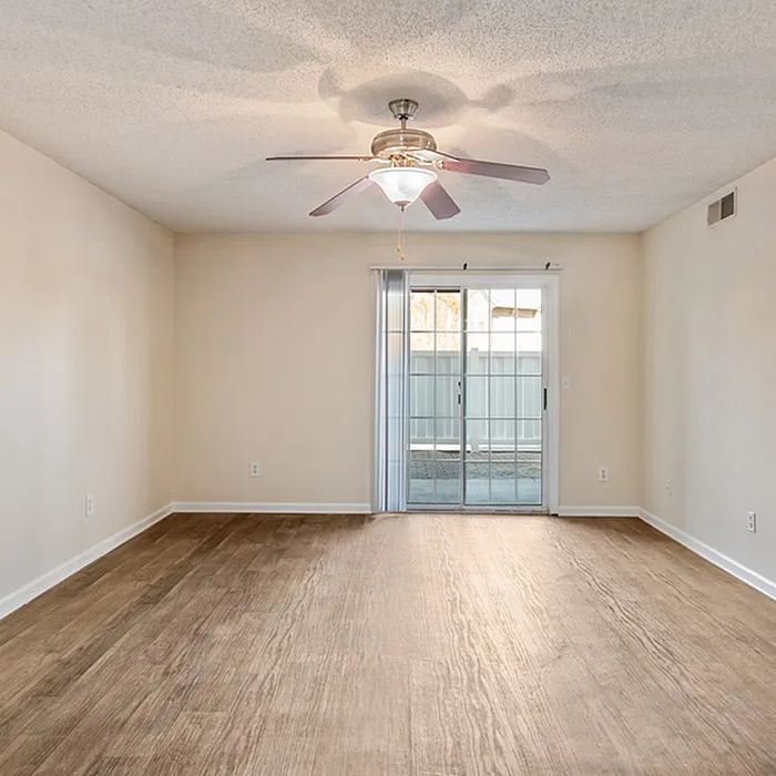 Bright empty room with elegant wood flooring, ceiling fan, and sliding glass doors leading to a serene patio space.