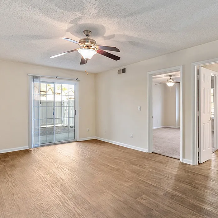 Bright and inviting living area with wooden flooring, modern ceiling fan, and sliding glass doors leading to a private patio.