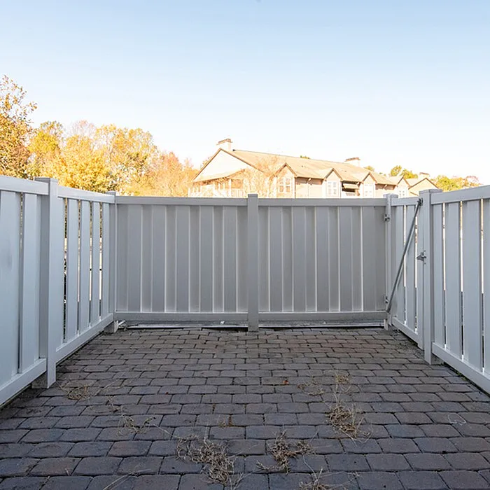 Charming outdoor patio with white privacy fence and rustic brick flooring, perfect for relaxing under a clear blue sky.