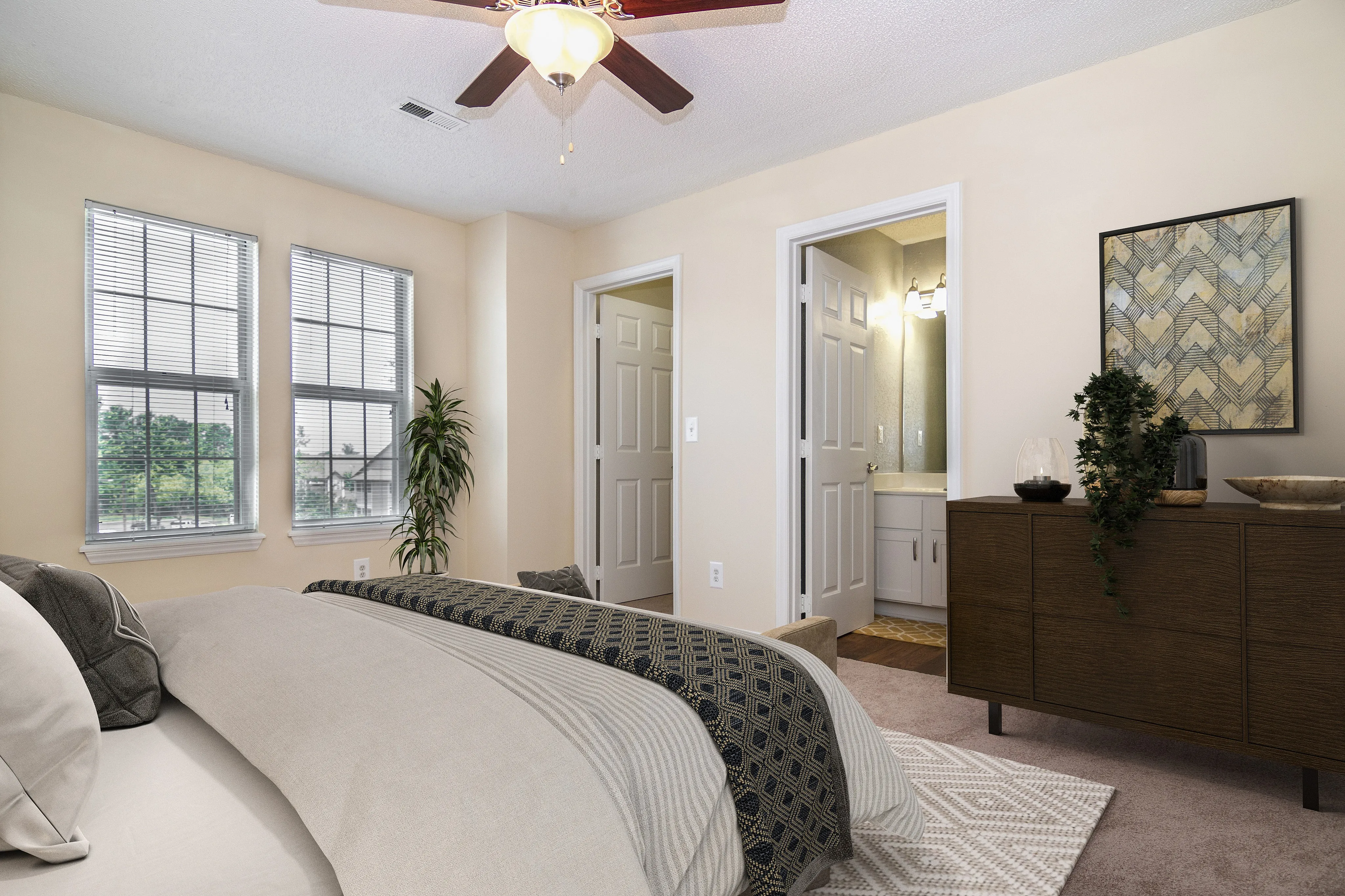 Elegant and cozy bedroom featuring a plush bed with stylish bedding, large windows for natural light, and modern decor with a view into a well-lit ensuite bathroom.