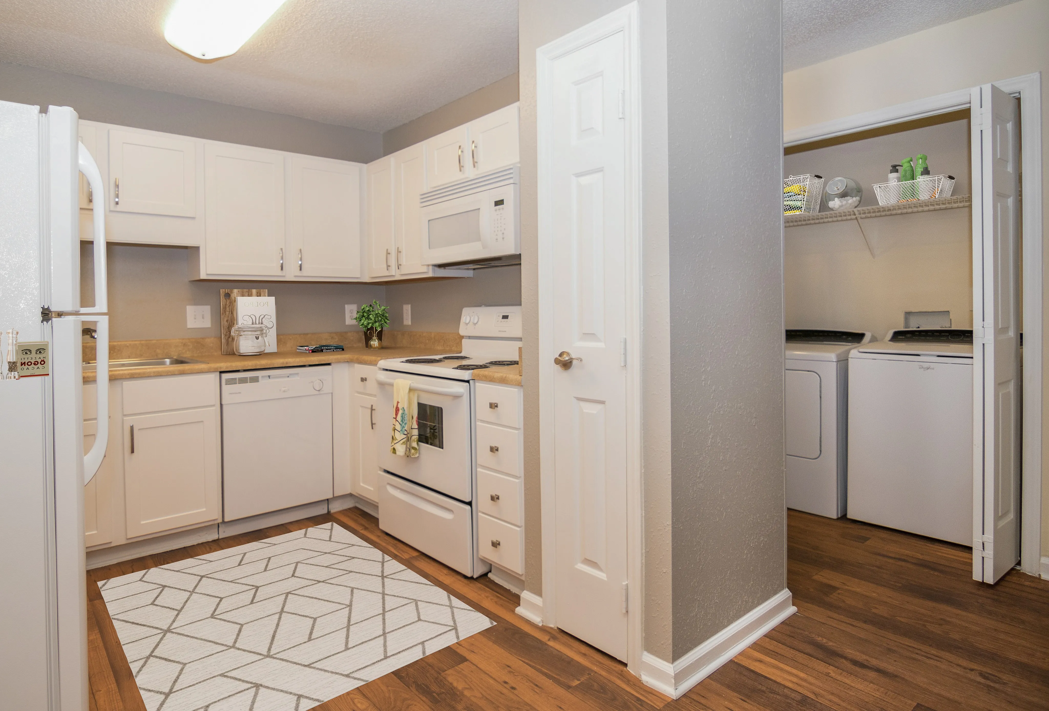 Bright kitchen with modern white cabinets, wood countertops, and sleek wood flooring, featuring adjacent laundry nook with washer and dryer.