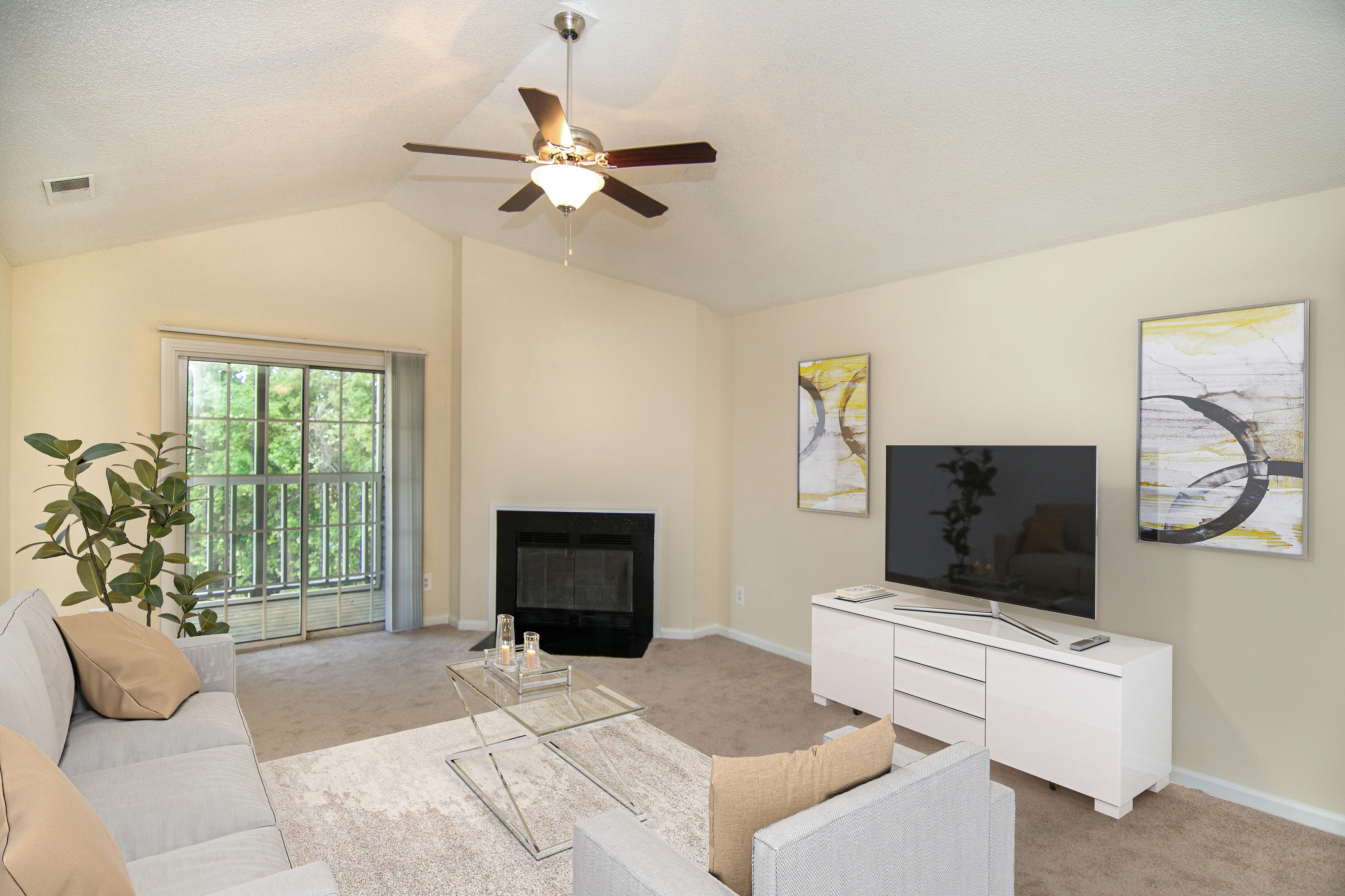 Bright and inviting living room with plush carpeting, modern furniture, large flat-screen TV, and a cozy fireplace, enhanced by natural light from a spacious window and patio door.