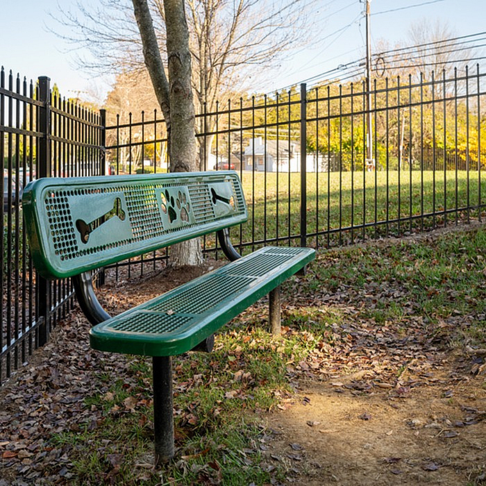 Charming outdoor space featuring a green bench with playful bone and paw designs, surrounded by lush greenery and a secure fence, perfect for pet-friendly relaxation.