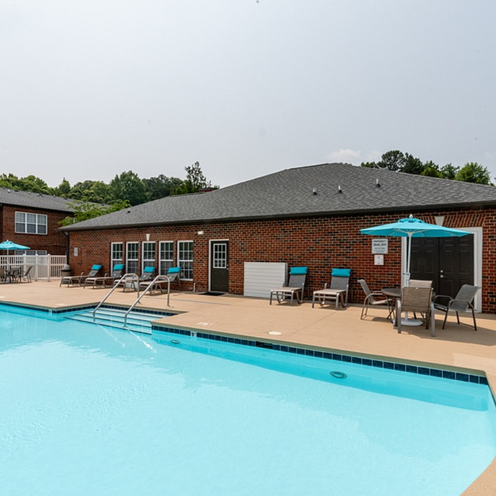 Charming brick apartment complex with an inviting swimming pool surrounded by cozy lounge chairs and umbrellas.