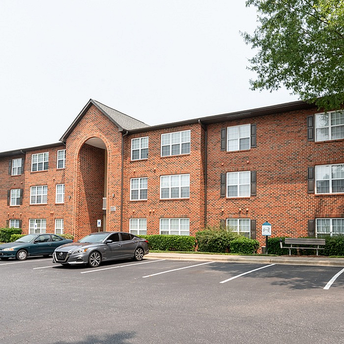 Charming red-brick apartment complex with ample parking and lush greenery, offering a welcoming and serene residential environment.