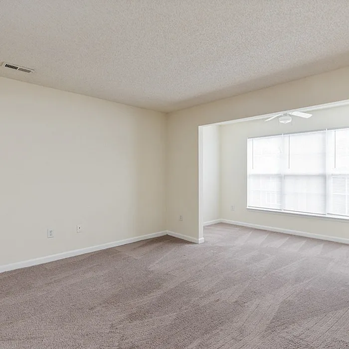 Bright and airy living space with plush carpeting, large windows, and modern ceiling fan, perfect for comfortable living.
