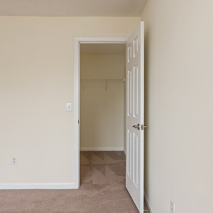 Spacious walk-in closet entry in a modern apartment with plush carpet flooring and neutral walls.