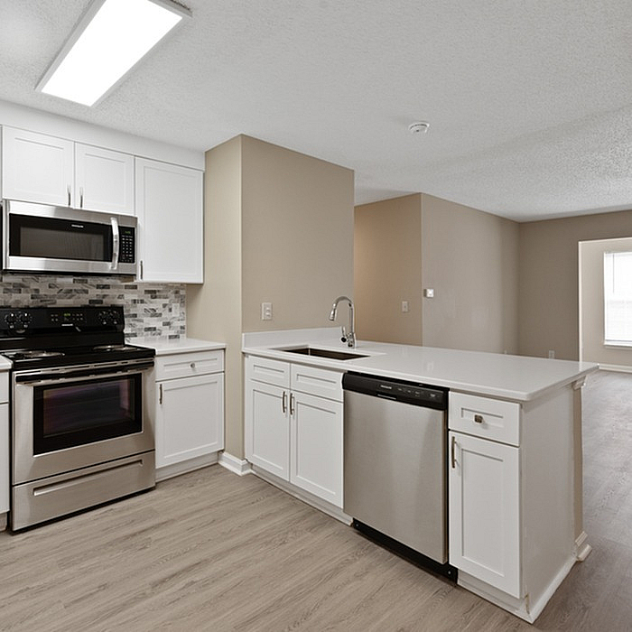 Modern kitchen with sleek stainless steel appliances, elegant white cabinetry, and a stylish backsplash, flowing into a bright open living area.