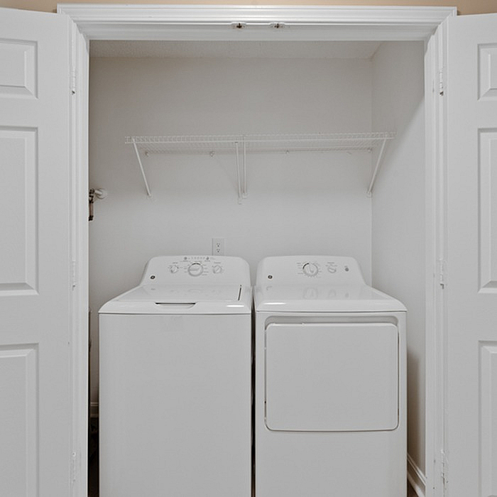 Compact laundry area with modern washer and dryer, enhanced by sleek white tones and handy storage shelving.
