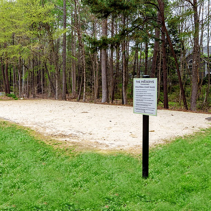 Serene outdoor sand volleyball court surrounded by lush greenery and tall trees, offering a perfect spot for recreation and leisure.