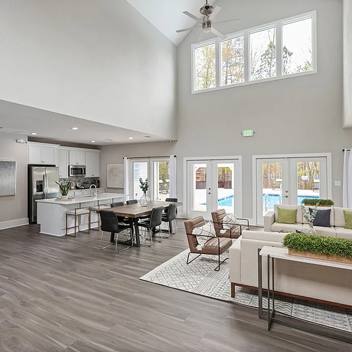 Modern open-plan living area with high ceilings, sleek kitchen, and cozy seating, overlooking a bright poolside view.