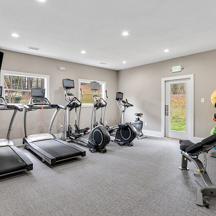 Modern fitness room with state-of-the-art treadmills, exercise bikes, and a weight bench, offering a bright and inviting workout space.