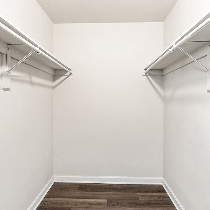 Spacious walk-in closet with white walls and elegant hardwood flooring, perfect for ample storage.