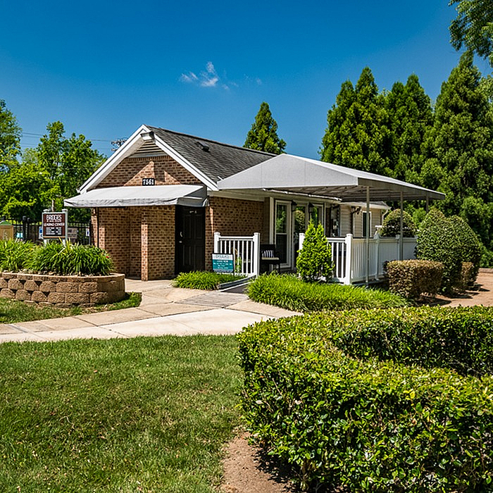 Charming brick apartment building with a welcoming porch and lush green landscaping, perfect for comfortable living.