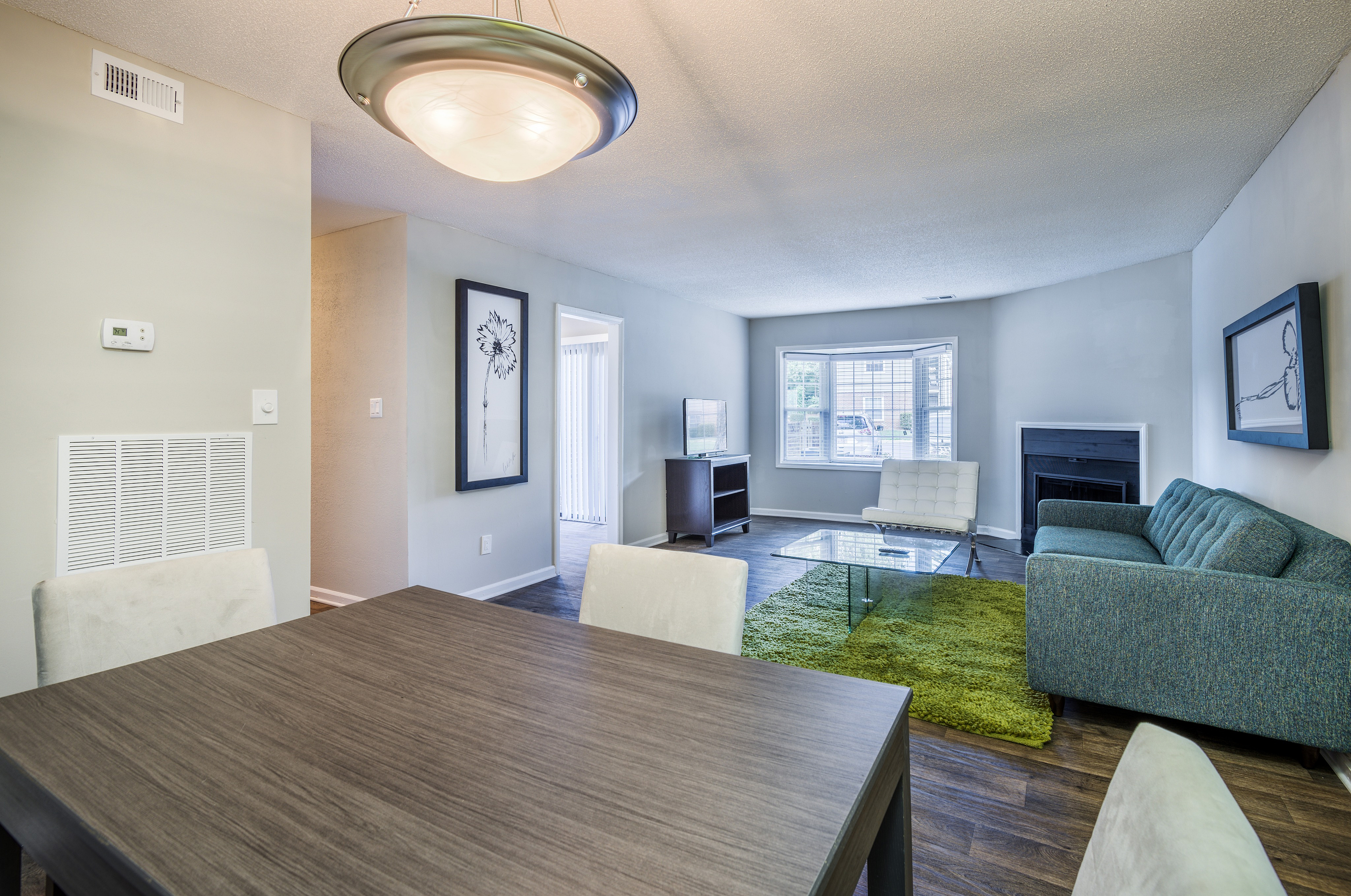 Modern living room with sleek gray sofa, stylish white chair, and glass coffee table on a vibrant green rug, featuring elegant artwork and a cozy fireplace.
