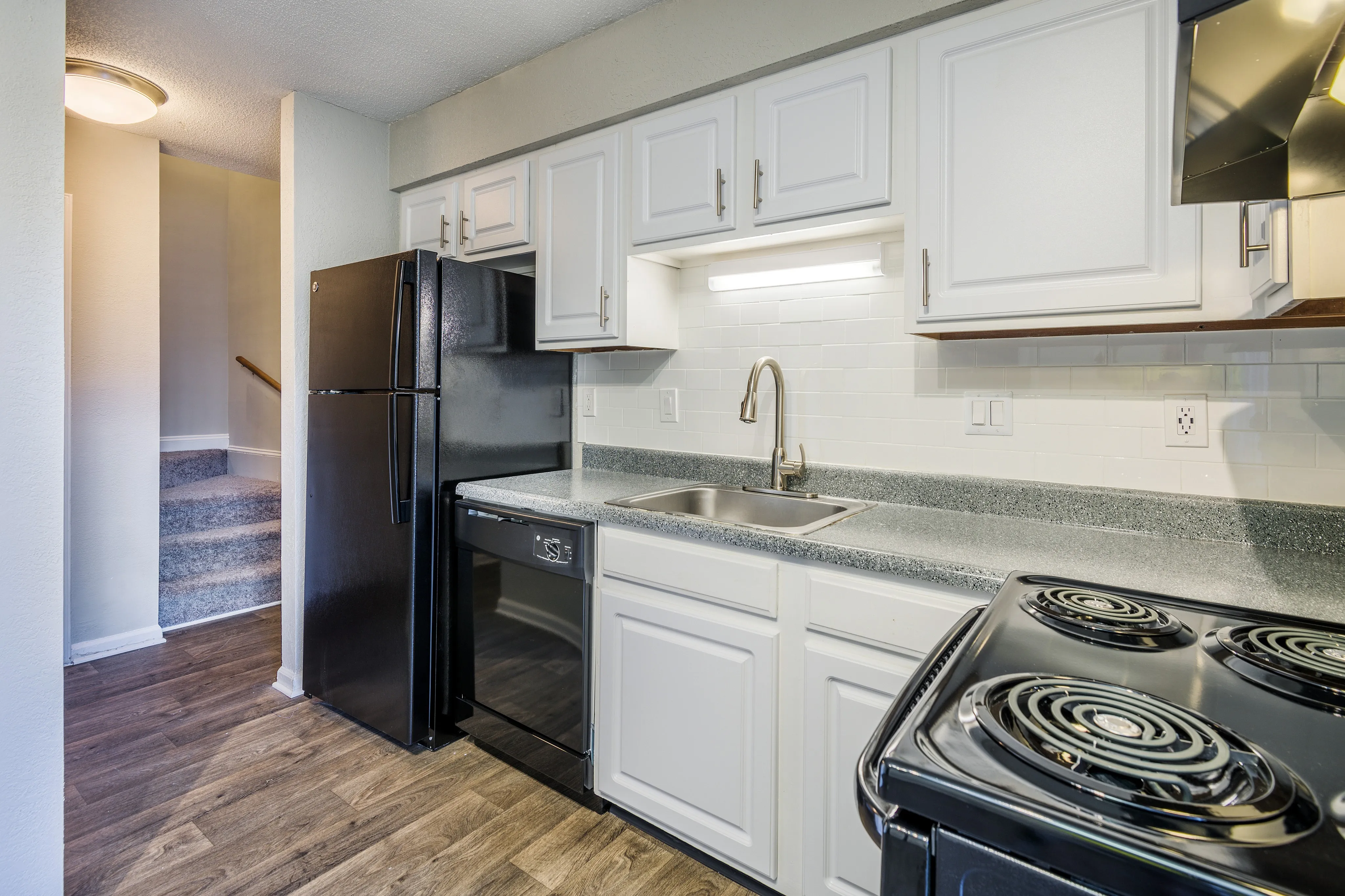 Modern kitchen with sleek countertops, white cabinetry, and black appliances, leading to cozy carpeted stairs.
