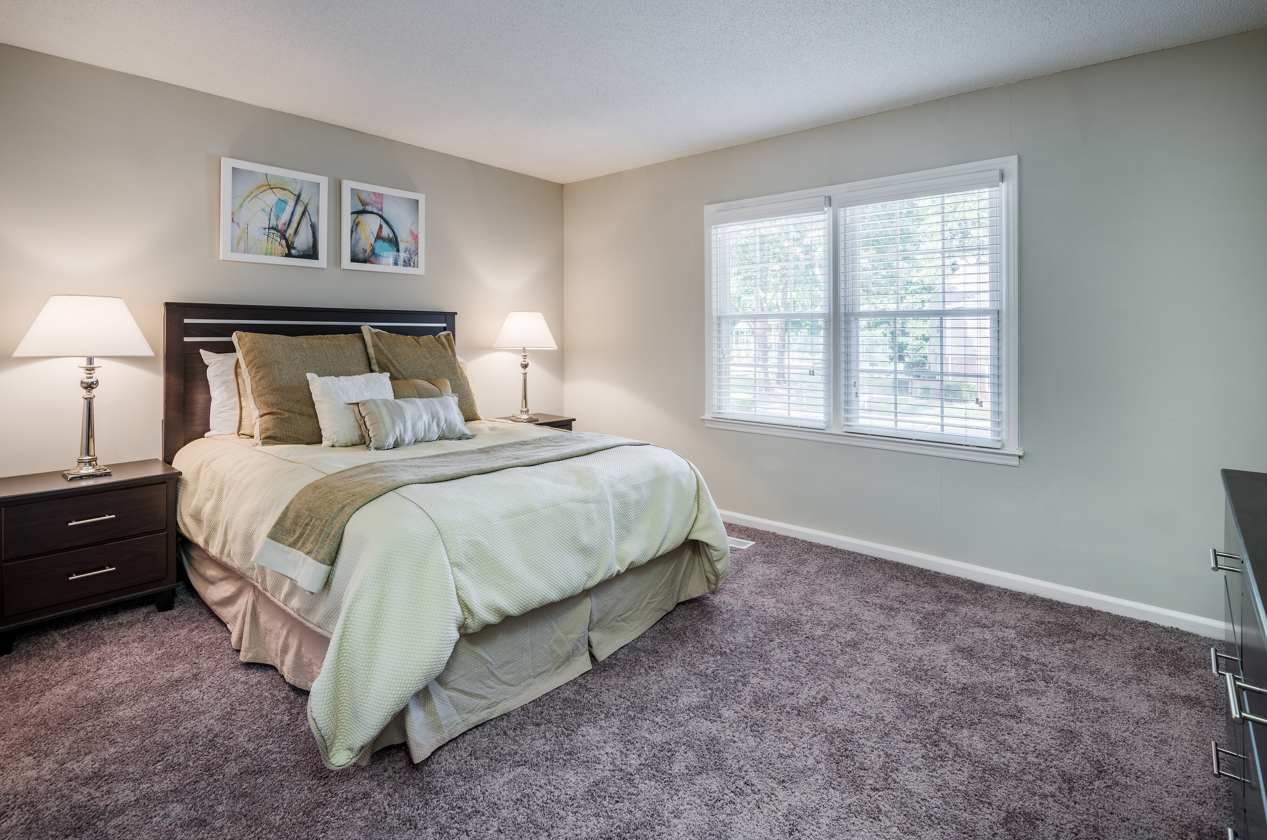 Inviting bedroom with plush carpet flooring, elegant bedding, and large window for natural light.