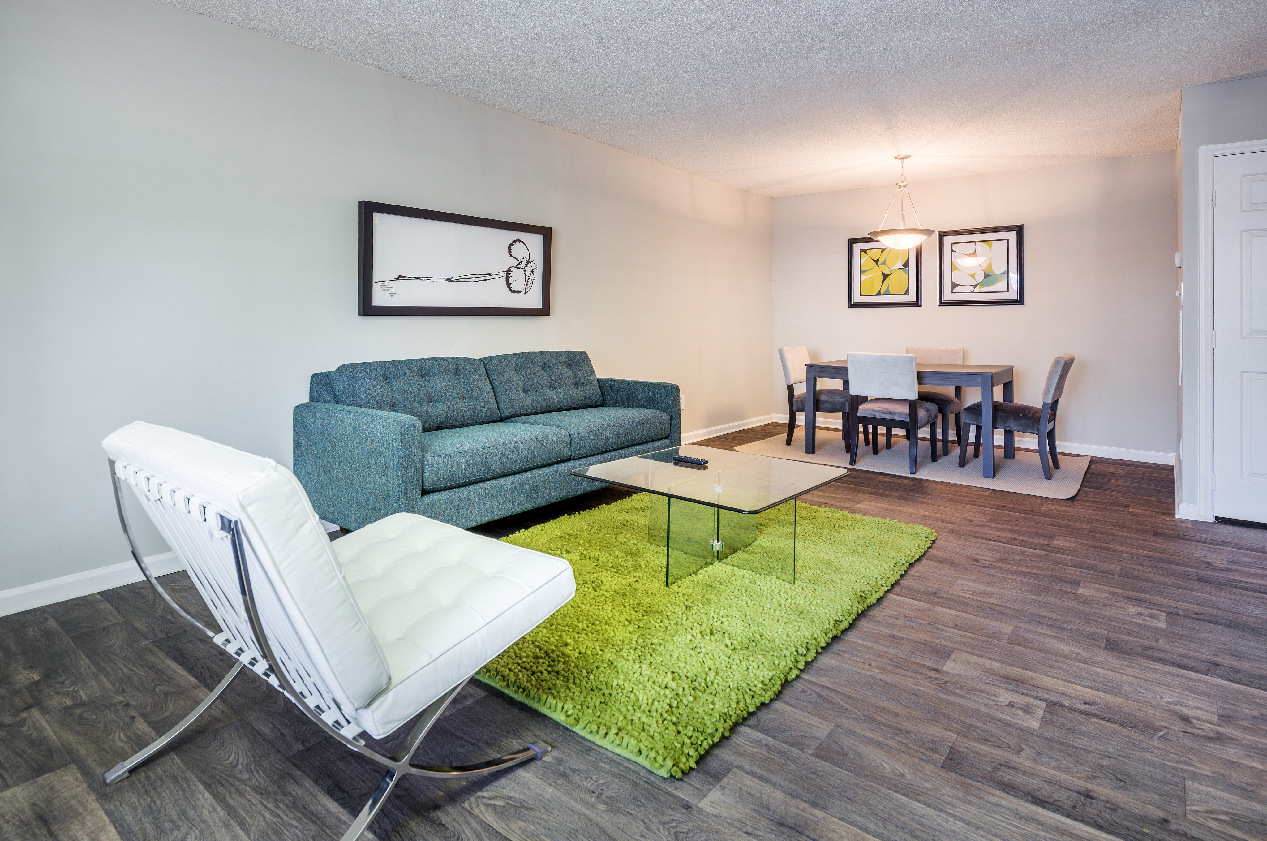 Contemporary living and dining area with sleek furniture, vibrant green rug, and elegant artwork.